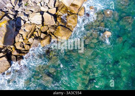 Immagine dall'alto verso il basso di una costa rocciosa che incontra il mare, con splendide acque verdi e vibrazioni estive, sfondo o carta da parati. Foto Stock