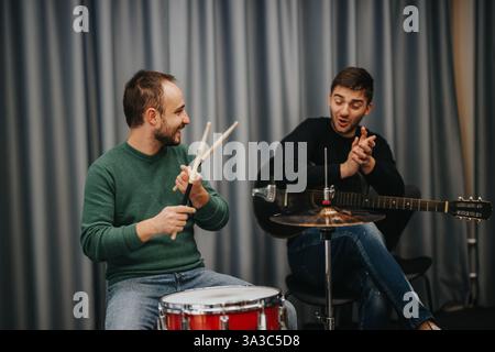 Due amici che praticano con gioia la musica insieme in un accogliente studio Foto Stock