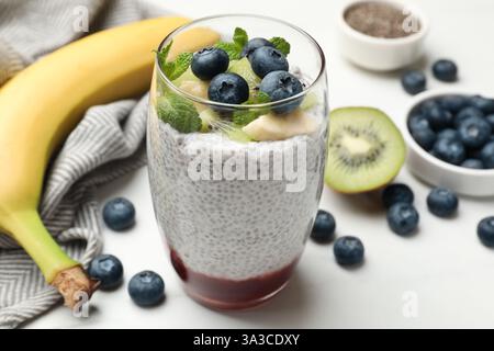 Delizioso budino di chia con mirtilli, kiwi, banana e menta in vetro su un tavolo leggero, primo piano Foto Stock