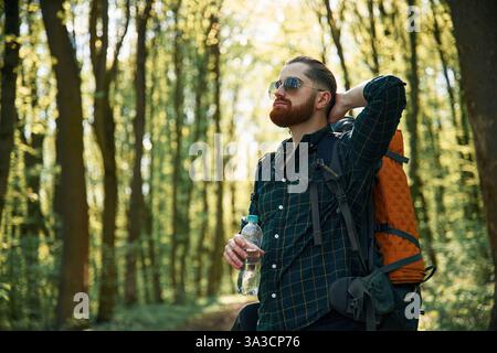Con zaino. L'uomo barbuto è nella foresta di giorno. Foto Stock
