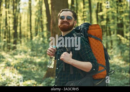 Bottiglia d'acqua, in attesa. L'uomo barbuto è nella foresta di giorno. Foto Stock