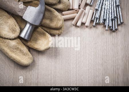 Pila di tasselli in legno martello a baionetta guanti da lavoro in pelle e chiodi in acciaio inox su tavola in legno Vista ravvicinata concetto di costruzione Foto Stock