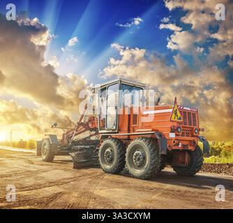 Trattore da costruzione d'epoca su ruote in piedi ai bordi della strada splendida vista del tramonto Foto Stock