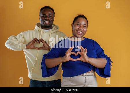Mostrando un gesto d'amore. La coppia nera felice è insieme su sfondo giallo. Foto Stock