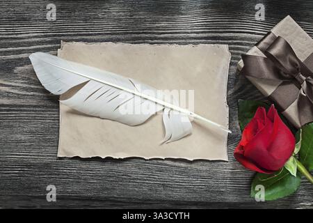 Foglio di carta vintage confezione regalo rosa rossa piuma su tavola in legno Foto Stock