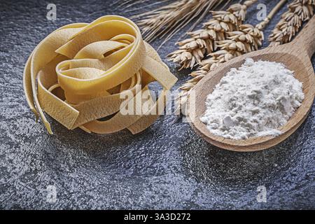 Orecchie di segale di frumento con cucchiaio di legno, pasta cruda su sfondo nero e concetto di cibo e bevande Foto Stock