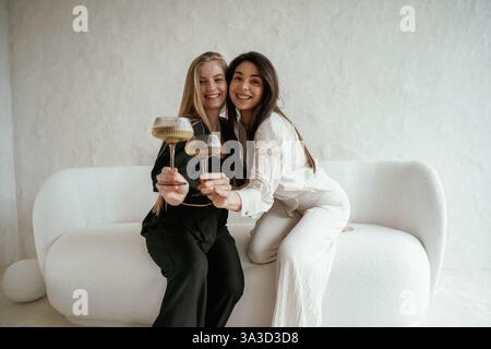 In bianco e nero, con drink, festeggiando. Due giovani amiche felici sono al chiuso. Foto Stock