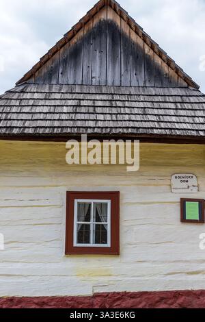 Vista frontale di una tradizionale casa in legno bianca con timpano in legno e piccola finestra a Vlkolinec, Slovacchia Foto Stock
