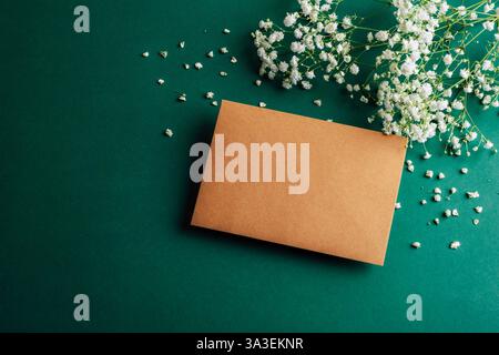 Busta marrone su sfondo verde con fiori bianchi di gypsophila. Vista dall'alto, posizione piatta, mockup. Foto Stock