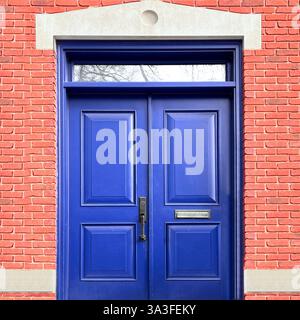 Doppie porte blu cobalto poste all'interno di una vibrante facciata in mattoni rosa, caratterizzate da una classica finestra sullo specchio di poppa e da eleganti dettagli architettonici. Foto Stock