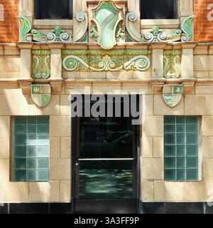 Un'entrata decorata dell'edificio presenta intricati dettagli in terracotta smaltata verde e oro, adagiati su una facciata gialla. Foto Stock