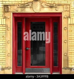 Ingresso rosso incorniciato da intricati dettagli in pietra su uno storico edificio in mattoni gialli a Chicago. Foto Stock