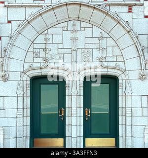Un paio di eleganti porte verdi con dettagli in ottone incastonate in un intricato arco in pietra intagliata con rilievi decorativi in stile medievale. Foto Stock