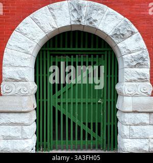 Un ingresso ad arco con cancello verde con una recinzione in legno, incorniciata da una storica struttura in pietra e mattoni rossi a Chicago. Foto Stock