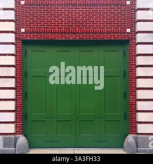 Una storica porta verde in stile carrozza posta all'interno di una facciata in mattoni rossi e pietra calcarea a Chicago. Foto Stock