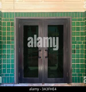 L'ingresso dell'edificio è situato all'interno di una suggestiva facciata di piastrelle verdi, che riflette il fascino architettonico vintage in un ambiente urbano. Foto Stock
