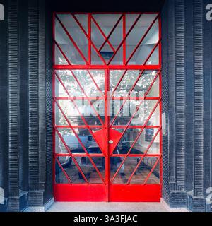 Ingresso modernista a Cracovia, Polonia, caratterizzato da porte in ferro con pannelli geometrici di vetro rosso poste all'interno di una facciata nera testurizzata, modernismo del XX secolo Foto Stock