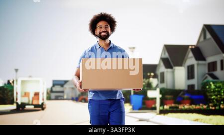 Corriere sorridente che consegna un pacco in un camion di servizio postale. Giovane in uniforme, in possesso di una scatola per la consegna Foto Stock
