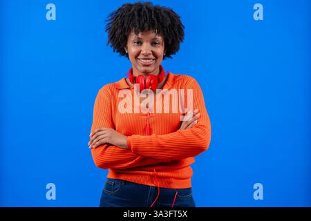 Donna afro-americana sorridente con cuffie rosse in posa su sfondo blu Foto Stock