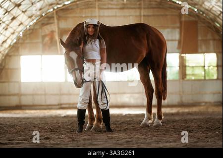 Nel cappello da cowboy. La bella giovane donna è con il cavallo al chiuso. Foto Stock