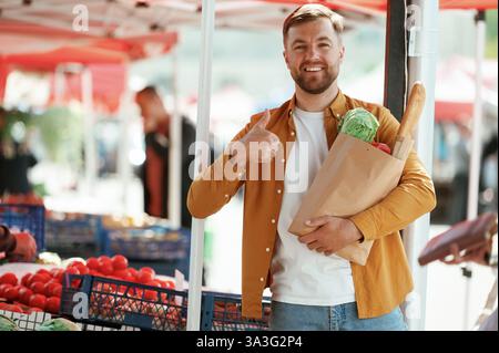 Raccolta dei prodotti in sacchetto di carta. Bell'uomo è al mercato di strada o al bazar. Foto Stock