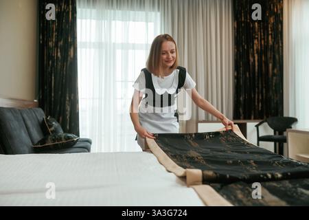 Mi prendo cura del letto. Una giovane cameriera è in camera. Foto Stock
