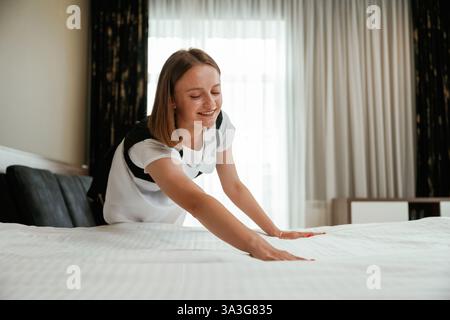 Occupato prendendosi cura del letto. Una giovane cameriera è in camera. Foto Stock