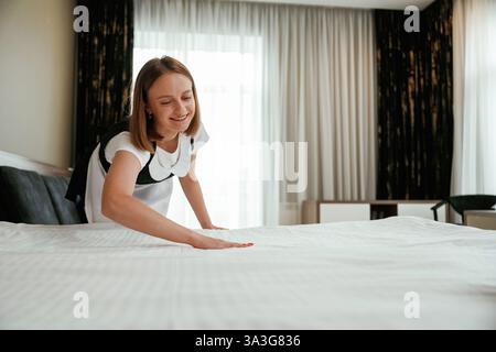 Occupato prendendosi cura del letto. Una giovane cameriera è in camera. Foto Stock