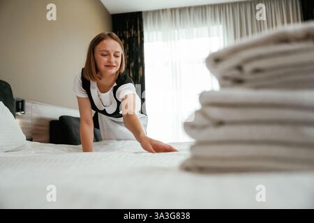 Occupato prendendosi cura del letto. Una giovane cameriera è in camera. Foto Stock