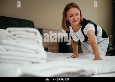 Occupato prendendosi cura del letto. Una giovane cameriera è in camera. Foto Stock