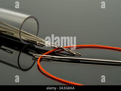 immagine ravvicinata di aghi da cucire grandi con gli occhi e il cotone arancione viene infilato attraverso un ago Foto Stock