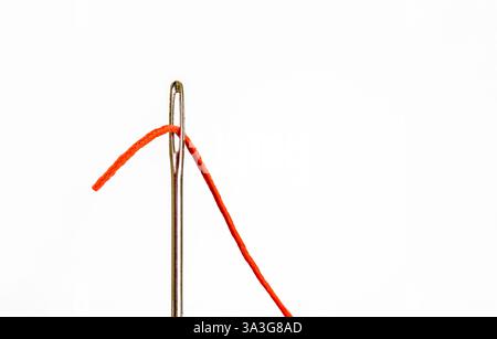 immagine ravvicinata di un grande ago da cucire con gli occhi e il cotone arancione infilato Foto Stock