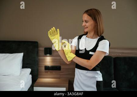 Indossare i guanti gialli. Una giovane cameriera è in camera. Foto Stock