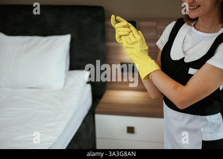 Indossare i guanti gialli. Una giovane cameriera è in camera. Foto Stock