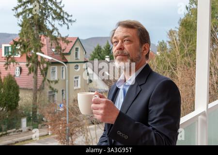 Un uomo elegante con una tazza di bevanda calda sorride mentre accoglie un nuovo giorno Foto Stock