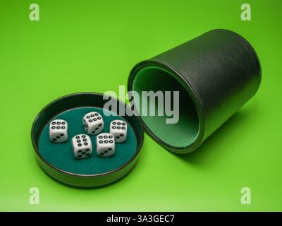 primo piano di cinque dadi bianchi che ne mostrano sei nel coperchio della tazza su sfondo verde Foto Stock
