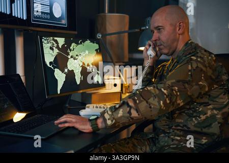 Ufficiale militare che monitora la sicurezza globale sugli schermi dei computer Foto Stock