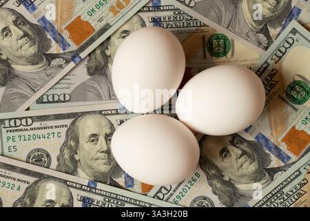 Le uova di gallina giacciono sui soldi, banconote da cento dollari sul tavolo, carenza di uova in America Foto Stock