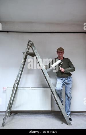 Pittore in abiti sporchi che posano contro la scala nel loft Foto Stock