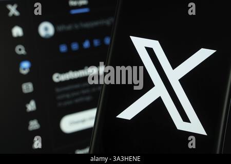 Il logo X (twitter) viene visualizzato su uno smartphone, con il sito Web bluesky visibile sullo schermo di un computer sullo sfondo Foto Stock