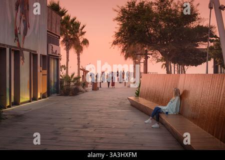 15 gennaio 2025, Abu Dhabi, Emirati Arabi Uniti: Giovane donna che gode il tramonto su una panchina sulla spiaggia di Hudayriyat Island Foto Stock