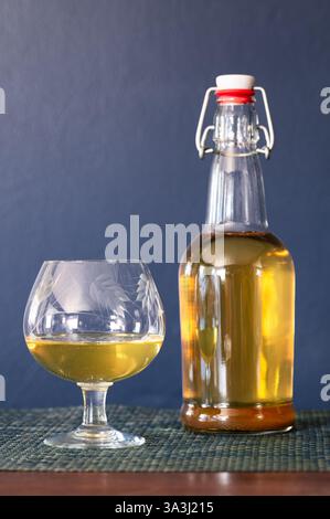 Un flacone trasparente con coperchio basculante e un bicchiere da cecchino pieno su un tavolo su sfondo blu scuro Foto Stock