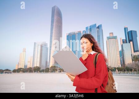 Giovane donna d'affari che rivede i suoi appunti con un'espressione sconcertata di fronte allo skyline di Abu Dhabi Foto Stock