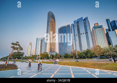 16 gennaio 2025, Abu Dhabi, Emirati Arabi Uniti: Turisti in bicicletta ad Abu Dhabi al tramonto con moderni grattacieli sullo sfondo Foto Stock