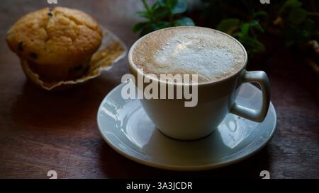 Un cappuccino e un muffin su un davanzale. Una pianta sullo sfondo. Foto Stock