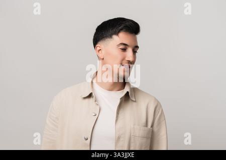 Cuffie mockup che fondono moda e tecnologia. Uomo elegante in una camicia beige che guarda verso il basso con un'espressione premurosa, ripreso in uno studio moderno Foto Stock