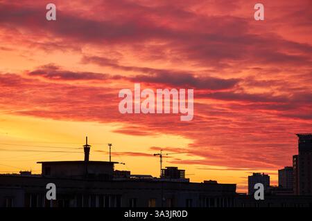 Una gru da costruzione si staglia contro un cielo rosso e arancione intenso. L'orizzonte luminoso crea un contrasto sorprendente con l'elem urbano scuro Foto Stock