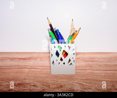 Una varietà di strumenti di scrittura sono disposti in modo ordinato in un elegante supporto, che mette in mostra un mix di colori e forme su uno sfondo chiaro Foto Stock