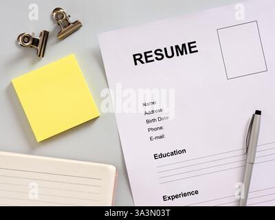 Riprendi, penna, blocco appunti e appunti disposti su una scrivania grigia, in attesa di essere compilati per le domande di lavoro Foto Stock