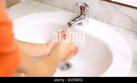 Uomo che sciacqua il sapone dalle mani sotto l'acqua corrente Foto Stock